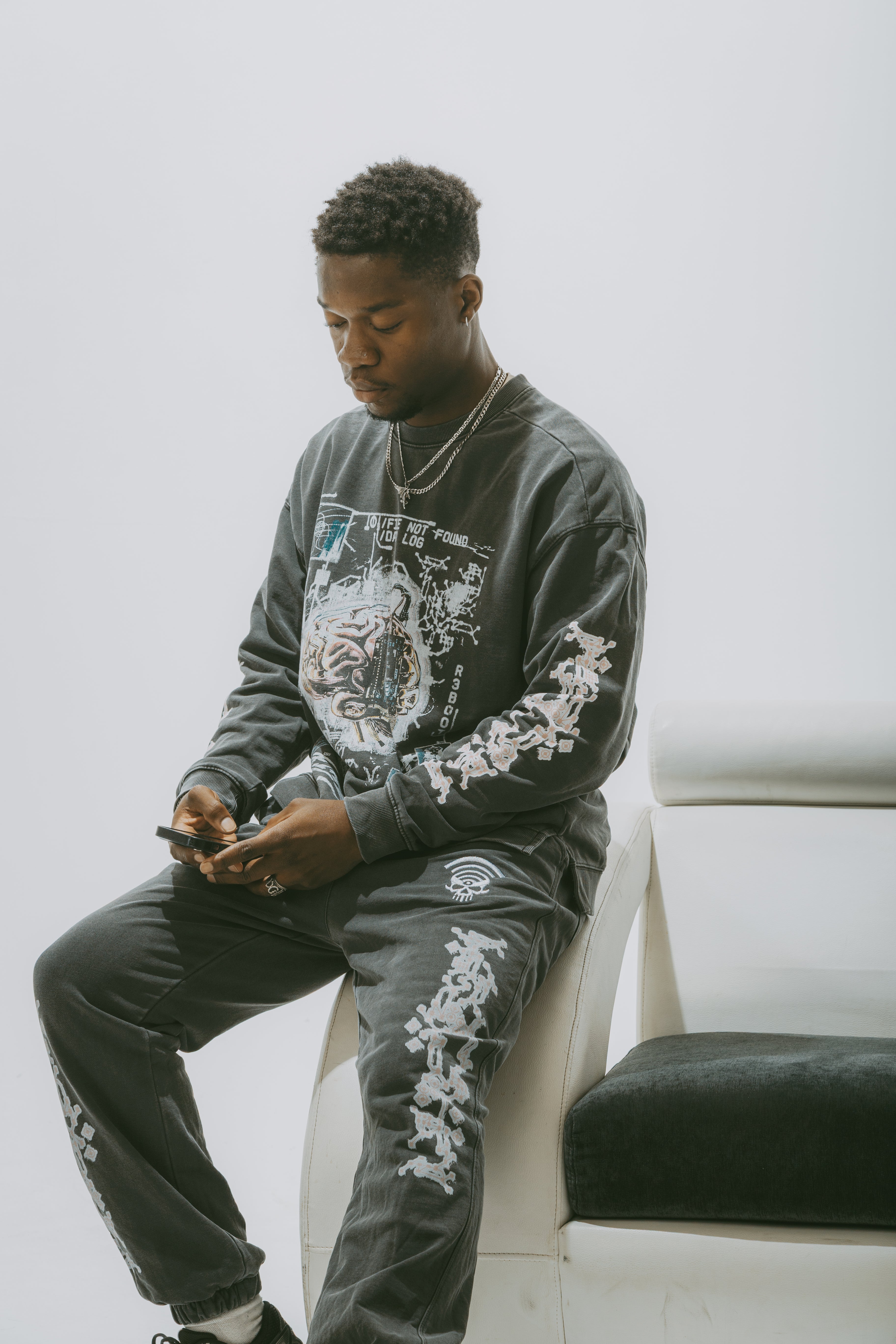 Man wearing Safe storage Drop Shoulder Sweater Grey, sitting on a chair and using a phone.